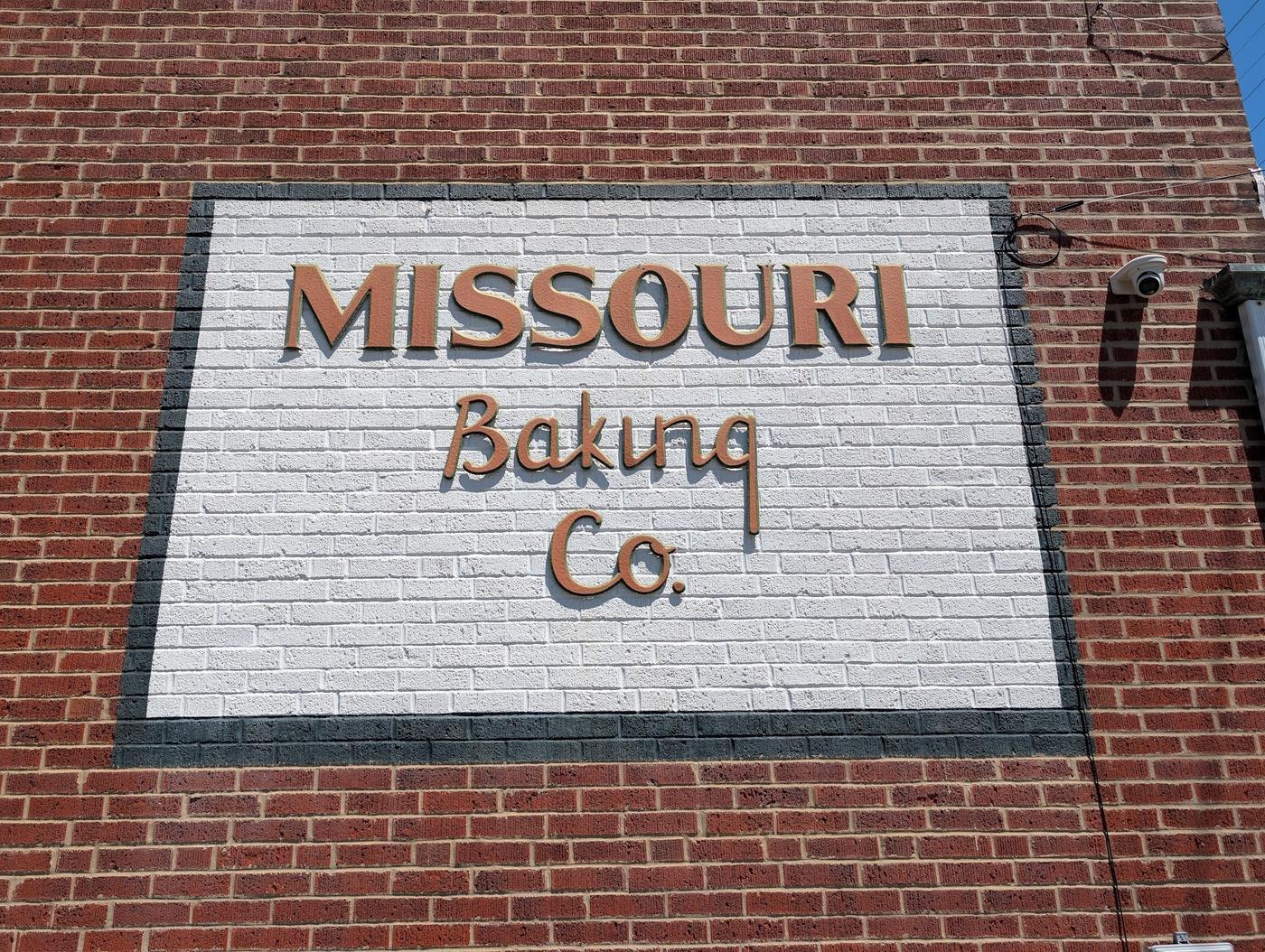The hand-painted Missouri Baking Co sign on the brick side wall of the bakery: block serif MISSOURI in terracotta over a script Baking Co.